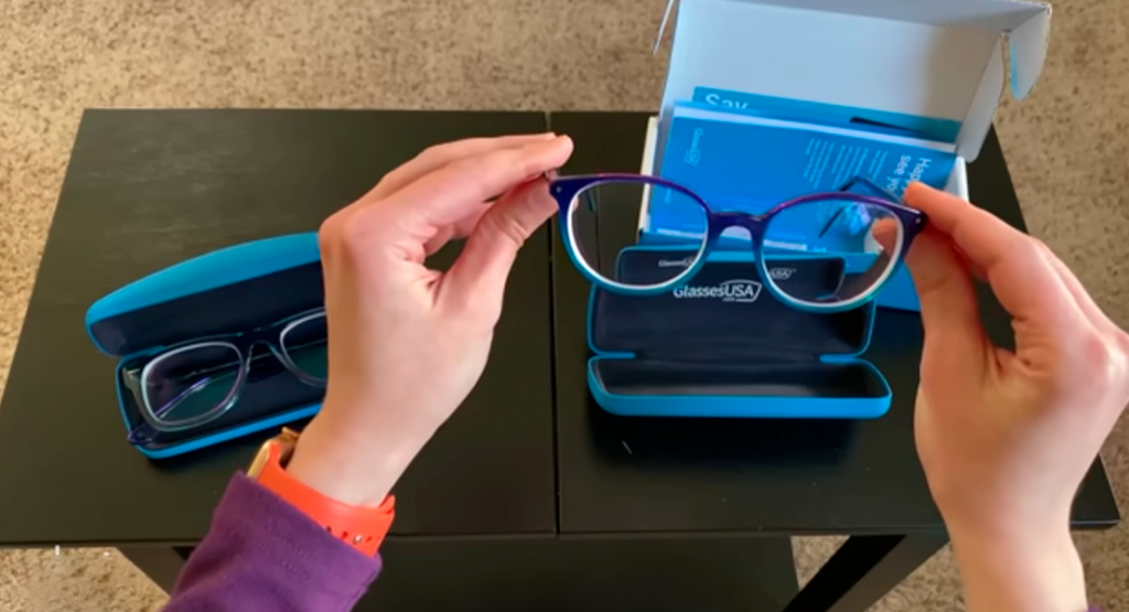 man's hands holding a pair of smart buy glasses over a black table with 2 blue smart buy cases and 1 box
